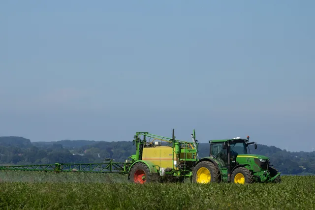 Green tractor spraying fertilizer on a vast agricultural field under clear blue sky. Pest Control Licence Requirements Ontario: Who Needs One