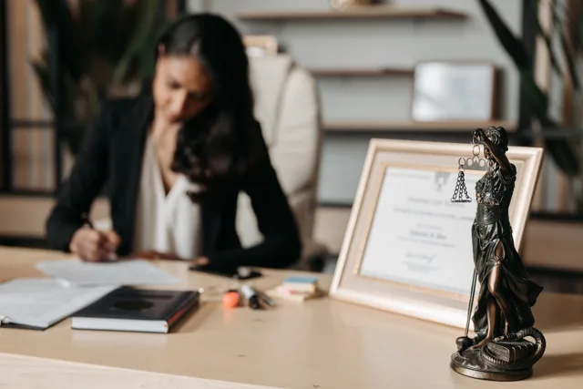 Focused woman writing at desk with Lady Justice figurine and certificate in office. Renew California Alcoholic Beverage Control License: Timing